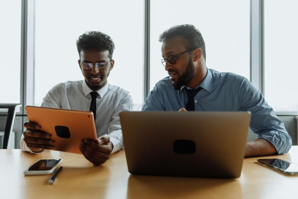 Two businessmen working together on digital devices in a modern office setting.